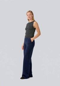 Top senza maniche grigio scuro con superficie testurizzata, abbinato a pantaloni larghi blu navy con tasche laterali e finitura liscia.