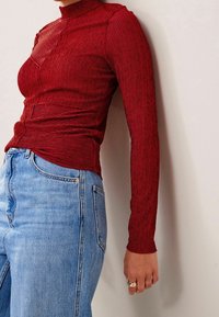 Top rosso a maniche lunghe con collarino e tessuto a righe. Abbinato a jeans in denim blu chiaro a vita alta.