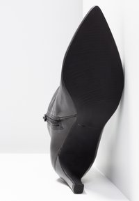 Stivale alto in pelle nera con tacco a spillo, punta affusolata, texture liscia e tacco sottile. Presenta cuciture sottili e una suola in gomma.