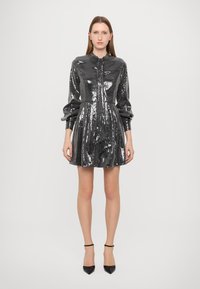 Abito di paillettes nere lucide con colletto a camicia, maniche lunghe e gonna svasata. Presenta bottoni frontali e dettagli drappeggiati.