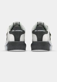 Λευκά αθλητικά παπούτσια με μαύρες λεπτομέρειες, λείο δερμάτινο υλικό, στρογγυλεμένο σχέδιο, χοντρή μαύρη σόλα και το λογότυπο "Karl Lagerfeld" στο πίσω μέρος.