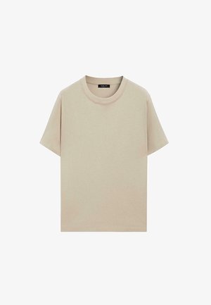 Beige T-shirt met korte mouwen en ronde hals, met zichtbare stiksels en een zwart merkembleem aan de binnenkant van de kraag.
