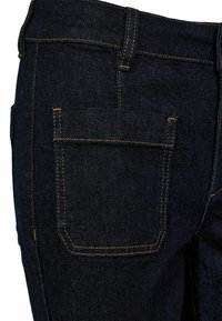 Jeans in denim blu scuro in primo piano che mostrano la tasca posteriore e i dettagli delle cuciture arancioni in vita e sulle cuciture.