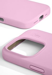 Svetlo roza etui za telefon z gladko mat površino, pravokotnimi izrezi za kamero in vhode ter vtisnjenim besedilom "IDEAL OF SWEDEN."