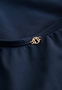 Marineblaues Netzgewebe mit glatter Textur, versehen mit einem gerafften Saum und einem goldenen runden Akzentdetail. Schlichtes und funktionales Design.