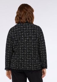Schwarze und goldene Tweedjacke mit strukturiertem Oberflächen, ausgefranstem Saum und lockerer Passform. Lange Ärmel und runder Ausschnitt.