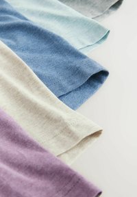 Bomullsduk i fem färger: ljuslila, beige, blå, ljusblå och grå, med en mjuk textur och rullade ärmsömmer.