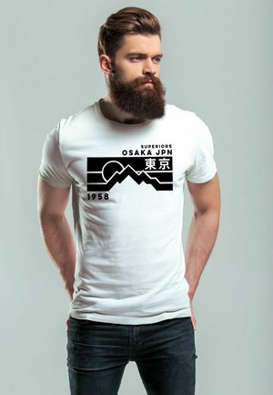 Weißes Baumwoll-T-Shirt mit einem schwarzen grafischen Design von Bergen und dem Text "SUPERIORS OSAKA JPN 1958" auf der Vorderseite. Darunter werden schwarze Jeans getragen.