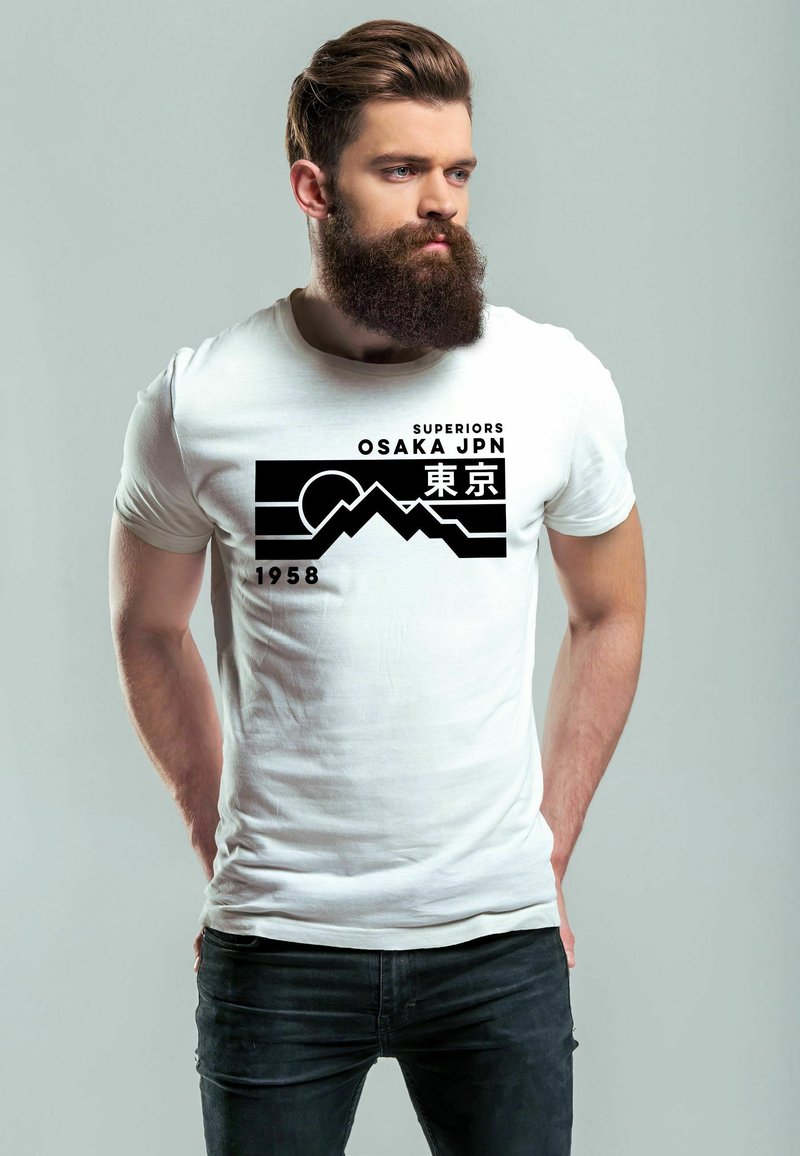 Weißes Baumwoll-T-Shirt mit einem schwarzen grafischen Design von Bergen und dem Text "SUPERIORS OSAKA JPN 1958" auf der Vorderseite. Darunter werden schwarze Jeans getragen.