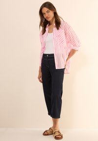 Růžová a bílá pruhovaná košile s knoflíky, bílý tílko, tmavé džíny a hnědé tkané sandály. Neformální outfit s volným střihem a kontrastními barvami.