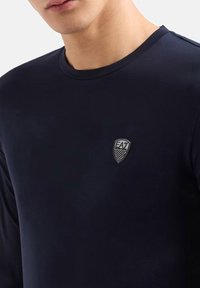 T-shirt a maniche lunghe di colore blu navy realizzato in un tessuto liscio, con un piccolo logo a scudo nero con strisce sul lato sinistro del petto.