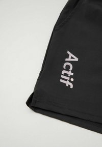 Μαύρο ύφασμα με λευκό κείμενο "Actif" τυπωμένο κοντά σε ραμμένο άκρο σε ένδυμα, πιθανώς σε μανίκι ή μπατζάκι παντελονιού.