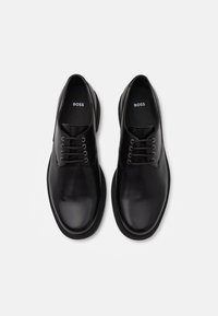 Scarpe eleganti in pelle nera con superficie liscia, punta rotonda e design con lacci. Presentano un marchio discreto sulle solette e una suola robusta.