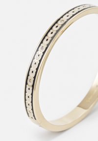 Bracciale in metallo dorato con una striscia nera decorata da un motivo bianco ripetuto e piccoli accenti di strass. Forma circolare, superficie liscia.