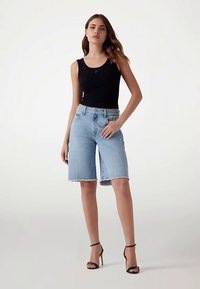 Pantaloni scurți Bermuda din denim albastru deschis, cu tiv tivuit, asortați cu un top negru fără mâneci și tocuri negre cu barete. Design cu picior drept.
