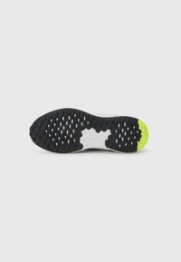 Semelle de chaussure présentant une base en caoutchouc noir texturé avec un accent blanc et jaune. Le design comprend des éléments de traction circulaires pour une meilleure adhérence.