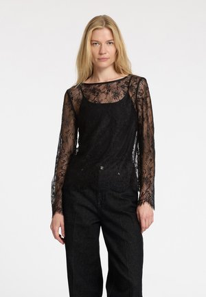 Zwarte kant lange mouwen top met een aansluitende binnenlaag, versierd met bloemmotieven en doorschijnende textuurmouwen. Gecombineerd met hooggepolsterde zwarte broek.