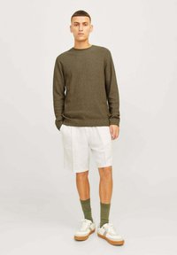 Pull en maille vert olive, short en lin blanc, chaussettes vertes et baskets blanches avec des accents beiges. Tenue d'été simple et décontractée.