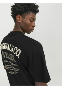 Sort t-shirt med korte ærmer, udstyret med hvid tekst på ryggen, der inkluderer mærkenavn og yderligere detaljer. Blød stofstruktur.