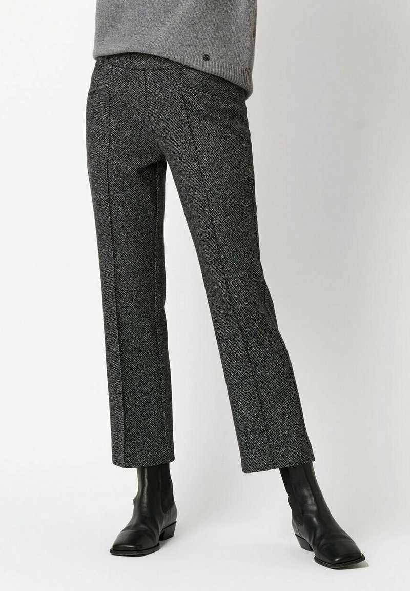 Dopasowane spodnie z czarno-szarego tweedu o prostym kroju nogawki, z subtelnymi teksturami i pionowymi szwami, zestawione z czarnymi botkami za kostkę.