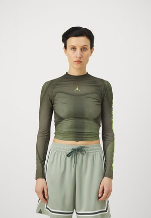 Long-sleeve, fitted athletic shirt in dark olive green with textured patterns and a contrasting neon green logo, paired with light gray shorts.