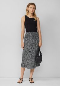 Čierny top bez rukávov skombinovaný s sukňou strednej dĺžky s bielym geometrickým vzorom. Modelka drží malú čiernu kabelku a má na sebe čierne sandále.