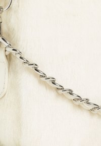 Collana d'argento con maglie intrecciate su una superficie bianca testurizzata, che mette in risalto una finitura liscia e una sottile lucentezza, contrastata dallo sfondo morbido.