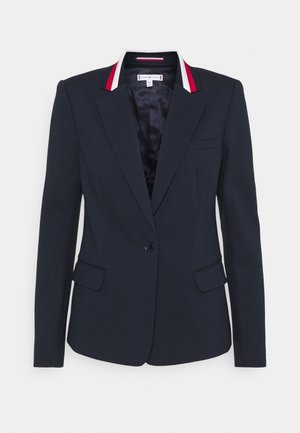 Marineblauwe, op maat gemaakte blazer met sluiting met één knoop, ingesneden revers, rood-witte streepdetails op de kraag en voorflappenzakken.