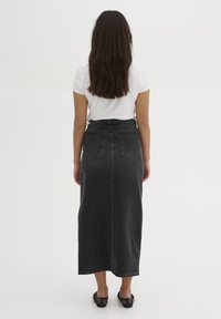 Gonna maxi in denim nero con taglio dritto, caratterizzata da due tasche posteriori e un leggero strappo all'orlo. Abbinata a una maglietta bianca.