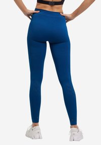 Leggings sportivi blu con vita alta, dettagli testurizzati sulla parte bassa delle gambe e scarpe da ginnastica bianche in contrasto. Il tessuto sembra elastico e aderente.