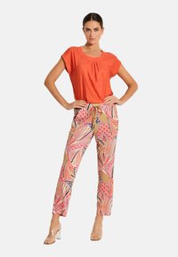 Rode top met korte mouwen en geplooide halslijn, gecombineerd met gestreepte broek in roze, oranje en zwart. Doorzichtige sandalen met blokhak complementeren de outfit.
