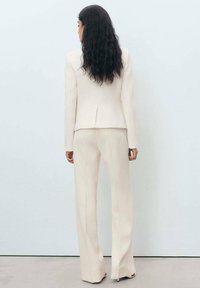 Beige maßgeschneiderter Blazer mit strukturierter Oberfläche, mit einer hinteren Schlitze, kombiniert mit passenden hoch taillierten, weiten Hosen. Glattes Stoff.