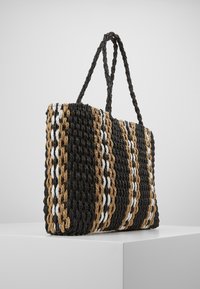 Wielbiona torba na ramię z wzorem w czarne, brązowe i białe paski. Prostokątny kształt z dwoma plecionymi uchwytami, wykonana z wytrzymałego, teksturowanego materiału.