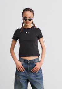 Tricou scurt negru, dintr-un material elastic, cu logo-ul alb Puma pe piept și cu legături decorative pe mâneci; asortat cu blugi cu talie înaltă.