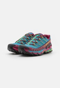 Ténis de trail running com um cabedal em azul e rosa, apresentando detalhes coloridos, uma sola texturizada e uma sola exterior de borracha preta durável.