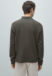 Polo a maniche lunghe verde oliva scuro con colletto, caratterizzata da un tessuto liscio e testurizzato e una vestibilità rilassata, vista da dietro.
