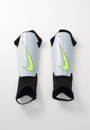 Grijze scheenbeschermers met een felgroen Nike-logo, voorzien van een glad plastic oppervlak en zwarte elastische banden voor een veilige bevestiging.