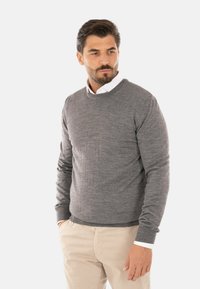 Maglione grigio a collo rotondo in tessuto morbido e testurizzato con maniche lunghe. Abbinato a pantaloni color crema; polsini visibili ai polsi.
