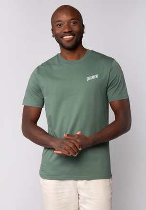 Groene katoenen t-shirt met korte mouwen en een ronde hals, met de tekst "GA GROEN!" in het wit op de linkerbovenhoek.