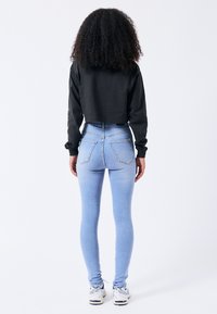 Sudadera negra recortada, jeans de tiro alto de color azul claro con bolsillos traseros, textura suave, combinados con zapatillas blancas.