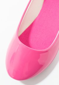 Chaussure plate en cuir laqué rose avec un bout rond et une semelle intérieure rose texturée. Surface lisse avec une finition brillante.