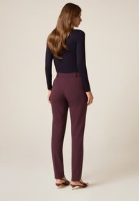 Zwarte lange mouwen top gecombineerd met aansluitende burgundy broek met een elastische tailleband, gladde stof en enkel-lange snit met minimale details.