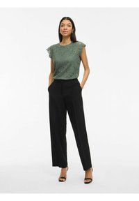 Groene kanten top met korte, geruffles mouwen, gecombineerd met hoge zwarte broek. Model draagt zwarte sandaaltjes met bandjes.