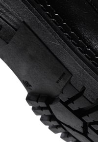 Gros plan d'une semelle de chaussure noire épaisse avec un motif de bande de roulement profond et des coutures visibles sur la partie supérieure en cuir.