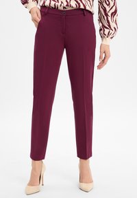 Burgundy tailored pants with a slim fit, belt loops, front pockets, and a smooth texture; paired with beige high-heel shoes.