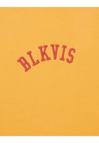Tela de algodón amarilla con bordado en relieve de color burdeos que forma la palabra "BLKVIS" en un diseño arqueado. Textura suave y apariencia casual.