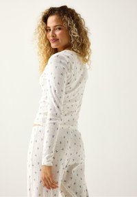 Hålsömsvit topp med långa ärmar och matchande byxor med blå blommönster; ribbad textur och figurnära design. Bakgrunden är helt vit.