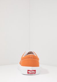 Baskets en toile orange avec semelle en caoutchouc blanche et couture. Présente un design bas et le logo "Vans Off The Wall" au niveau du talon.