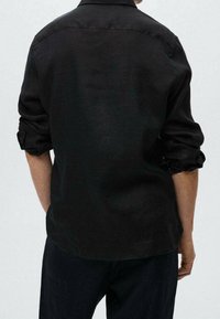 Camisa de lino negra con mangas enrolladas, que presenta un cuello clásico y un diseño limpio y sencillo. Textura suave con un peso ligero.