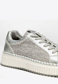 Sneaker argento caratterizzato da un corpo in tessuto grigio testurizzato, dettagli metallici e una suola in gomma bianca rigata con cuciture visibili.